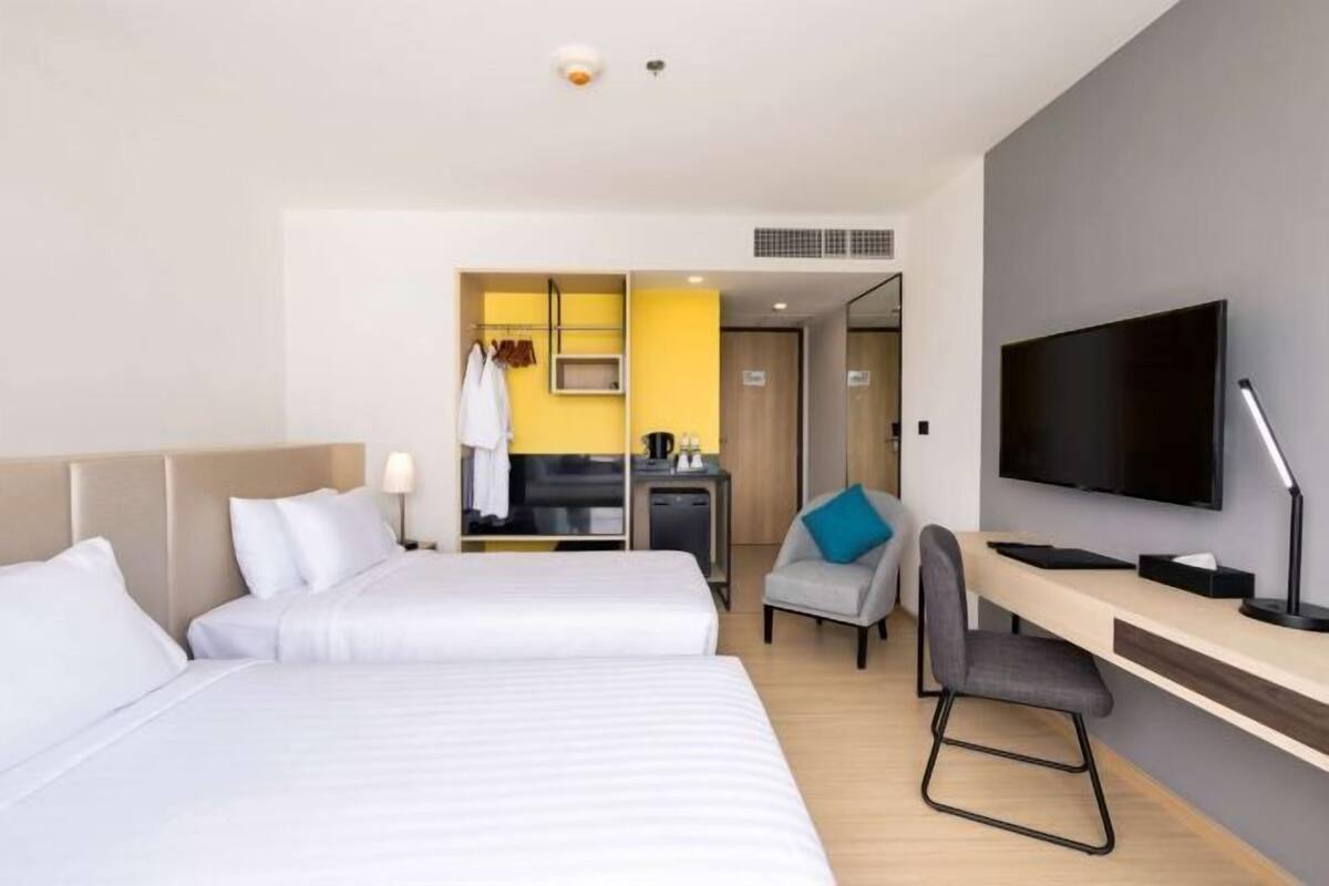 A hotel room with two beds, a desk, a TV, and a kitchenette.