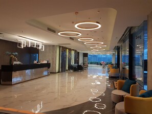 A modern lobby with a reception desk, seating area, and large windows offering a view. - Best Western Nada Don Mueang Airport Hotel (Bangkok)