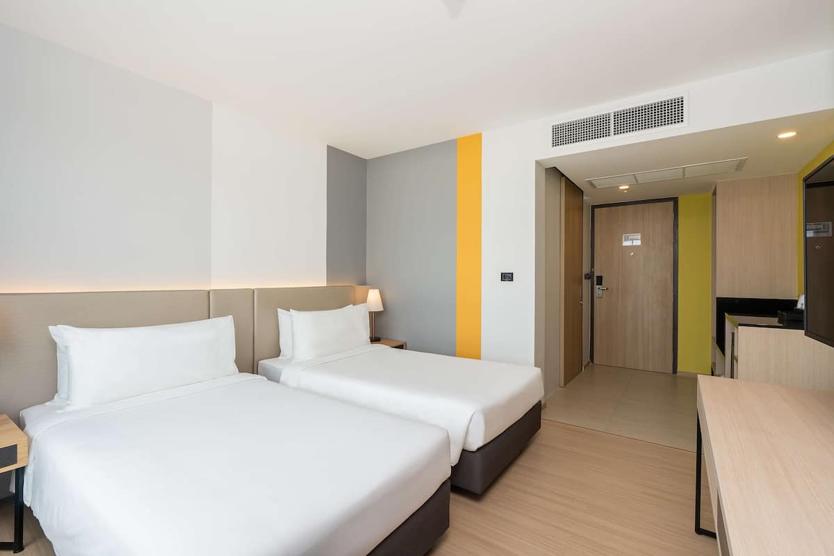 A hotel room with two beds, a desk, and a kitchenette.