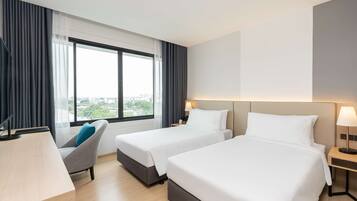 Habitación de hotel con dos camas, un escritorio, una silla y un ventanal con vistas a la ciudad.