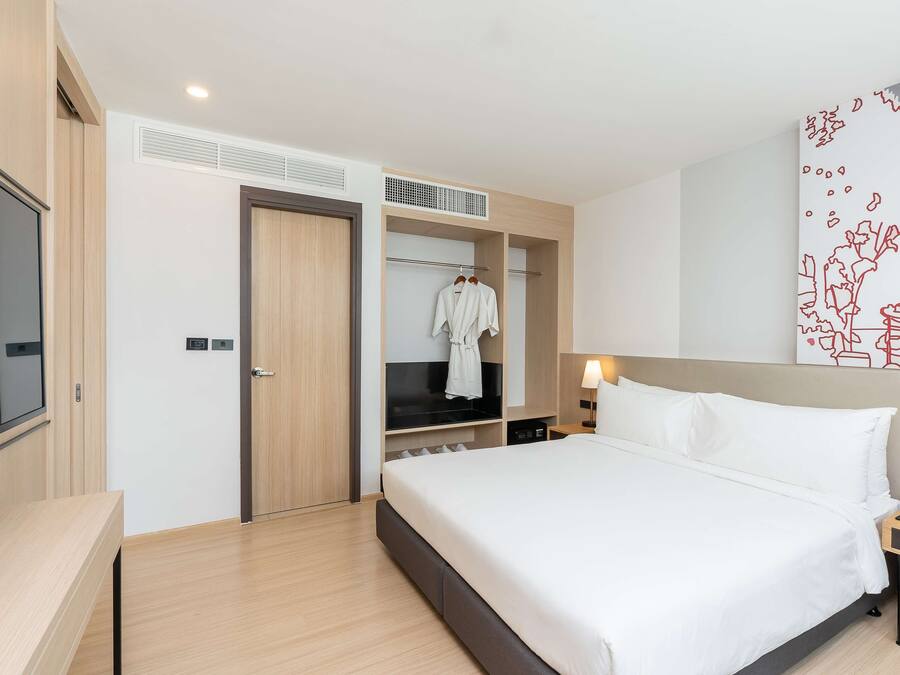A hotel room with a bed, bedside table, lamp, and a wardrobe with a TV.