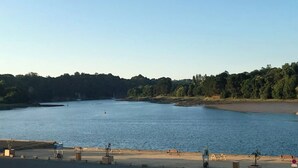 Une vue sur la côte, avec une plage de sable, une eau calme et une colline boisée en arrière-plan.