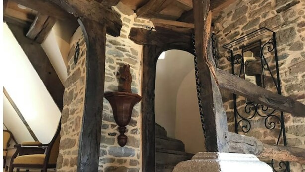Une pièce aux murs de pierre, dotée d’un plafond en bois, d’une cheminée en pierre et d’un lustre en métal.