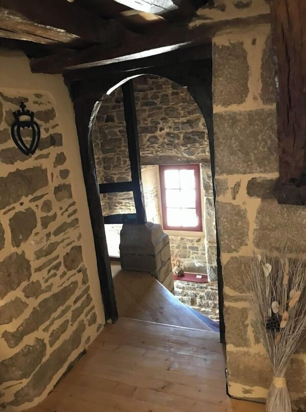 A stone-walled corridor with a wooden floor, a window with red trim, and a stone bench.
