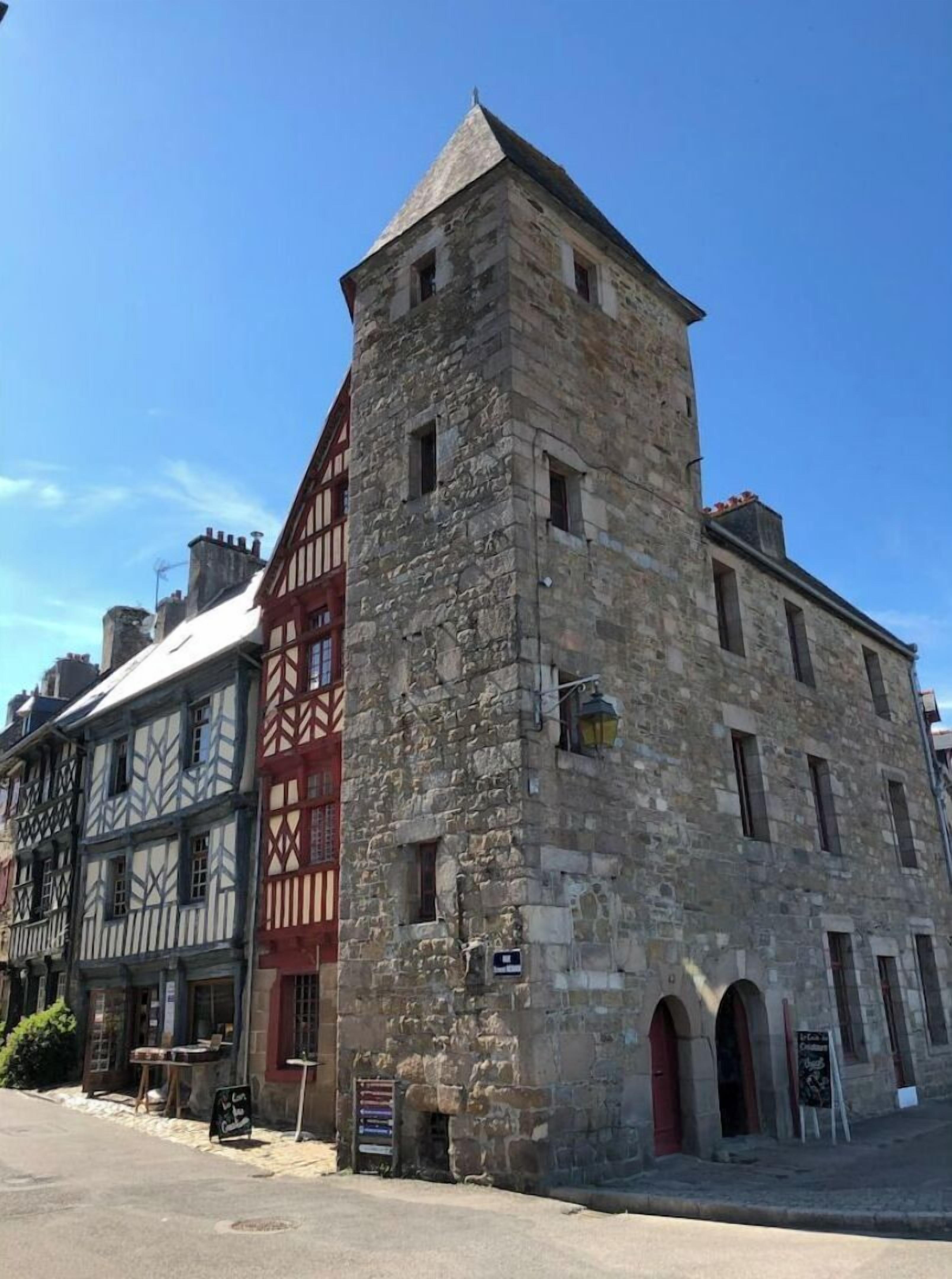 Un edificio de piedra histórico con una torre destacada y una estructura tradicional de entramado de madera adyacente.