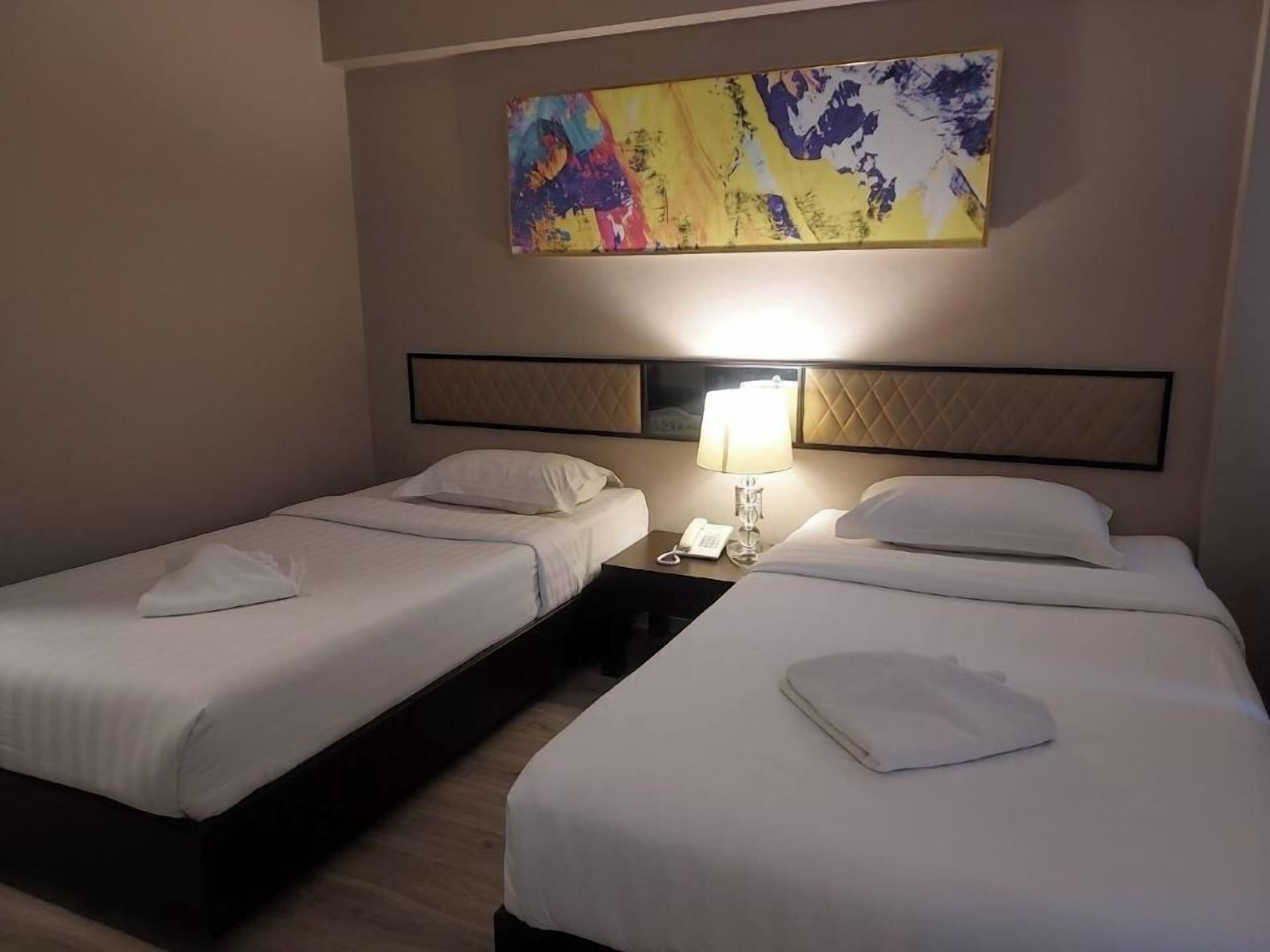 A hotel room with two beds, a nightstand with a lamp, and a colorful abstract painting on the wall.