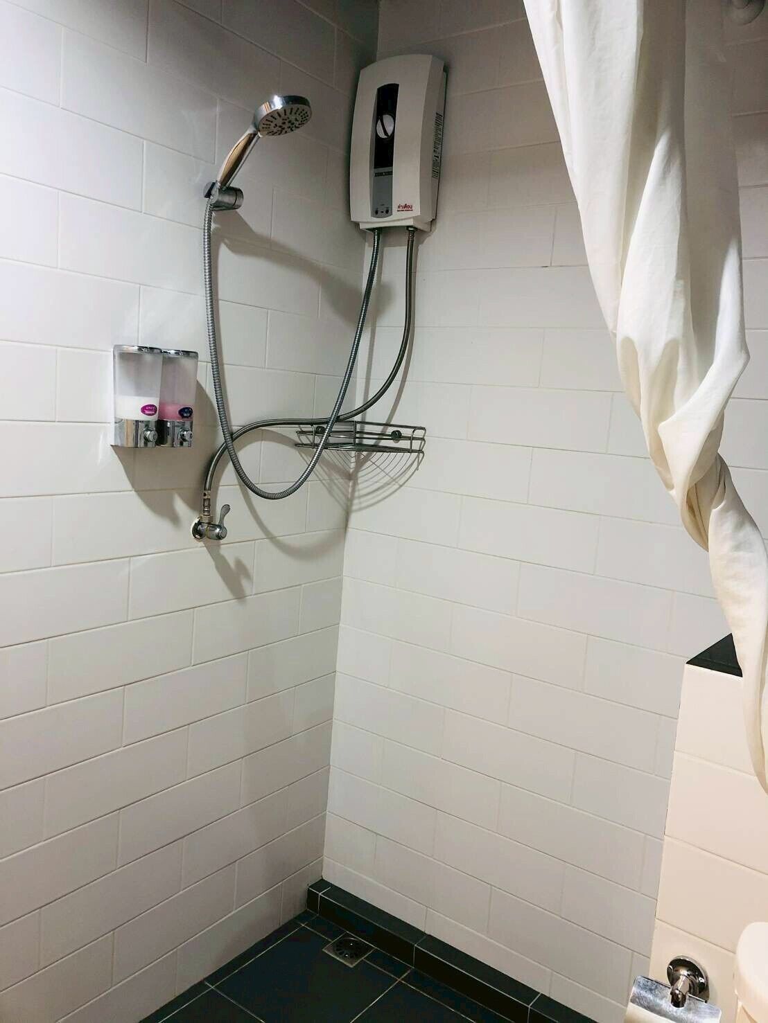 A shower area with a handheld showerhead, a wall-mounted water heater, and a towel rack.