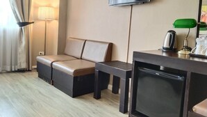 A hotel room with a sofa, a small table with a kettle, a TV, and a lamp. - Taris Art Hotel Phrae (Phrae)