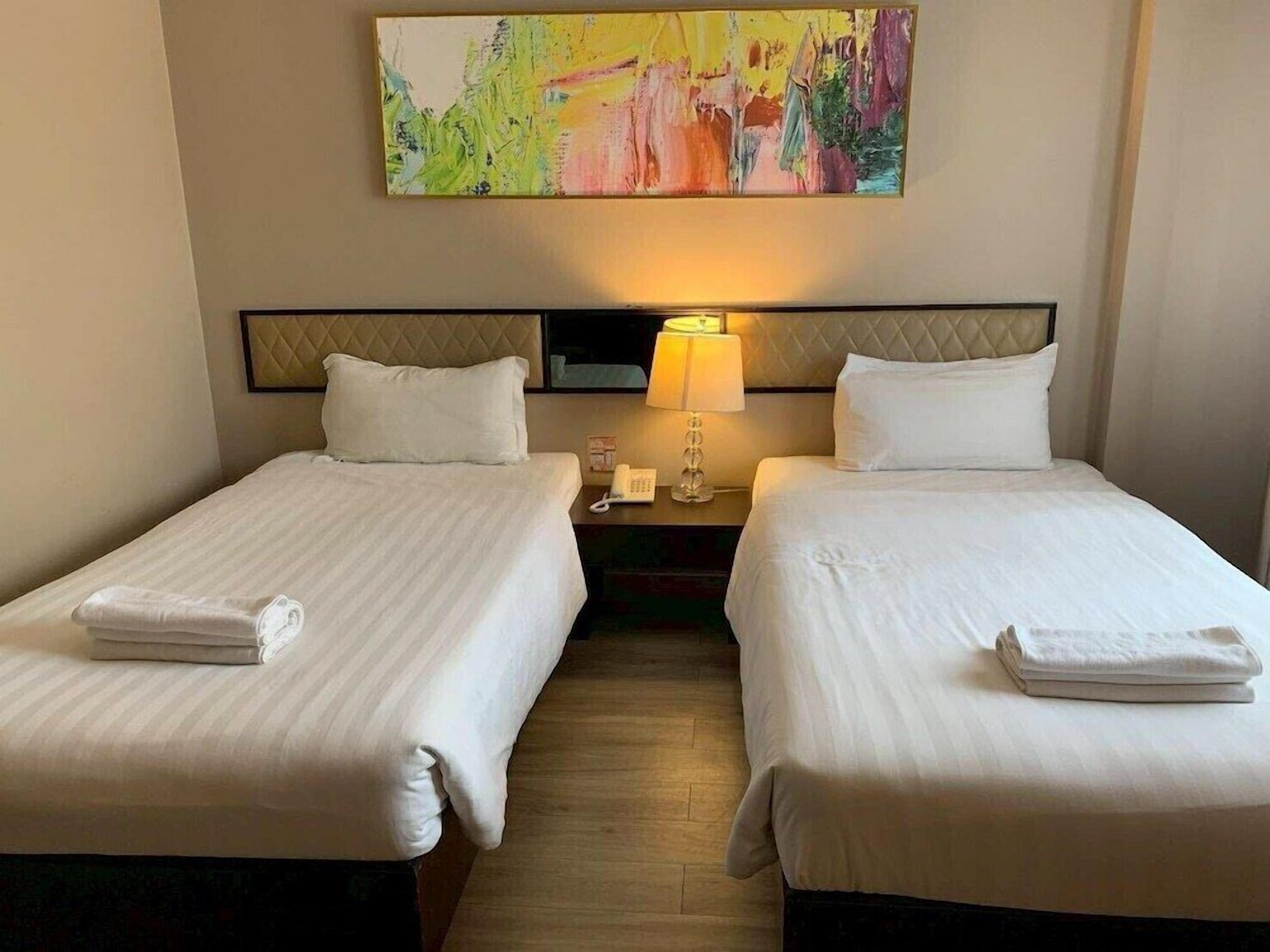 Habitación de hotel con dos camas, un cuadro en la pared, una lámpara de noche y un teléfono en la mesita de noche.