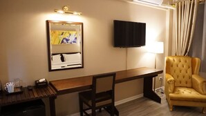A hotel room with a wooden desk, a chair, a flat-screen TV, a mirror, and a lamp. - Taris Art Hotel Phrae (Phrae)