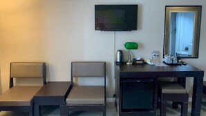 A hotel room with a flat-screen TV, a desk with a lamp, chairs, and an air conditioning unit. - Taris Art Hotel Phrae (Phrae)