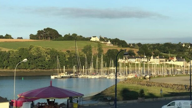 A marina with boats, a small dockside café, and a hill with buildings in the background. - Appartement de Charme "Le Bureau des Armateurs" (Tréguier)