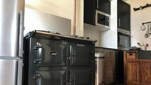 A kitchen with a large black stove, a stainless steel refrigerator, wooden cabinets, and a microwave. - Appartement de Charme "Le Bureau des Armateurs" (Tréguier)
