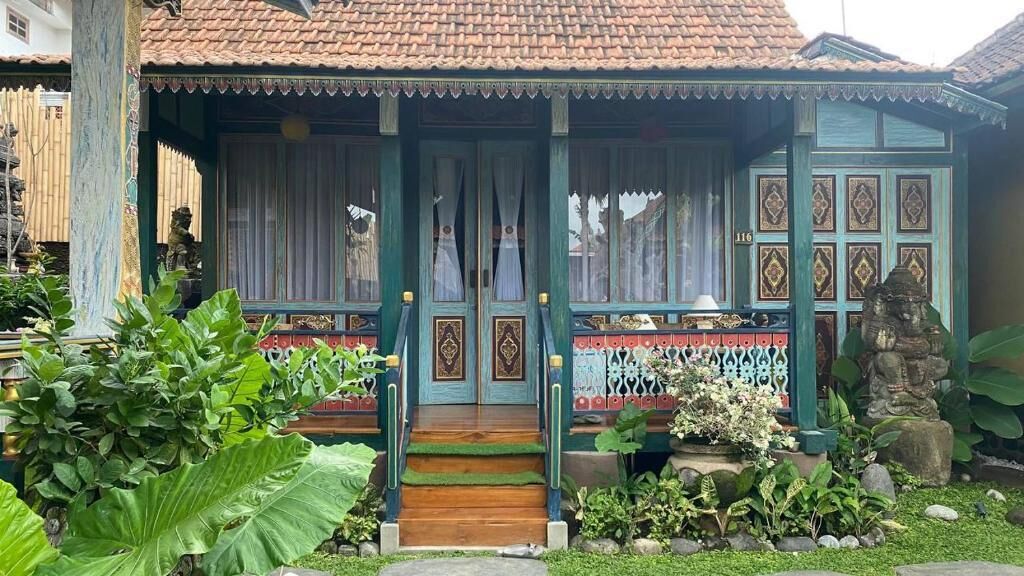 A traditional house with a tiled roof, a porch with a wooden staircase, and a garden with various plants.