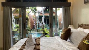 Ein Hotelzimmer mit Bett, Blick auf einen Swimmingpool und einen tropischen Garten.