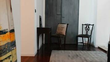 Una habitación con piso de madera oscura, un tapiz estampado, dos sillas de madera y una puerta oscura.