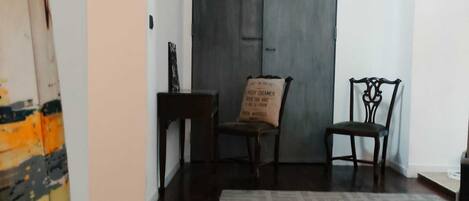 Una habitación con piso de madera oscura, un tapiz estampado, dos sillas de madera y una puerta oscura.