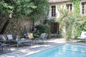 Un área junto a la piscina con sillones de descanso, un muro de piedra y un edificio con ventanas.