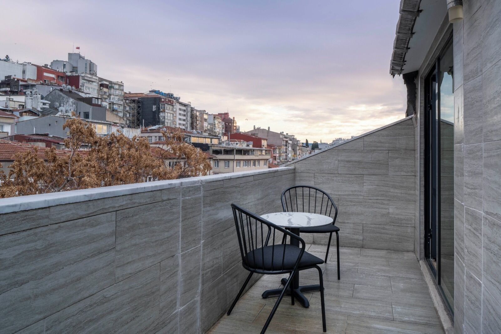 A balcony with a table and chairs, a cityscape view, and a tiled wall.