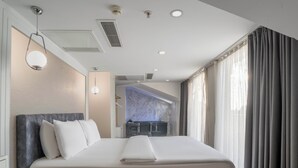 A modern hotel room with a large bed, a bedside table, a built-in desk, a bathroom with a sink and mirror, and a view of the city through large windows. - actuel life hotel (Istanbul)