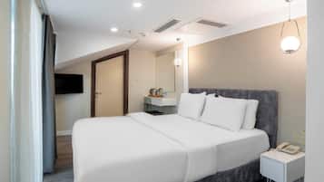 A modern hotel room with a large bed, a bedside table with a phone, a small desk with a mirror, and a ceiling light fixture.