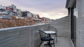 A balcony with two chairs and a table, overlooking a cityscape with buildings and trees.