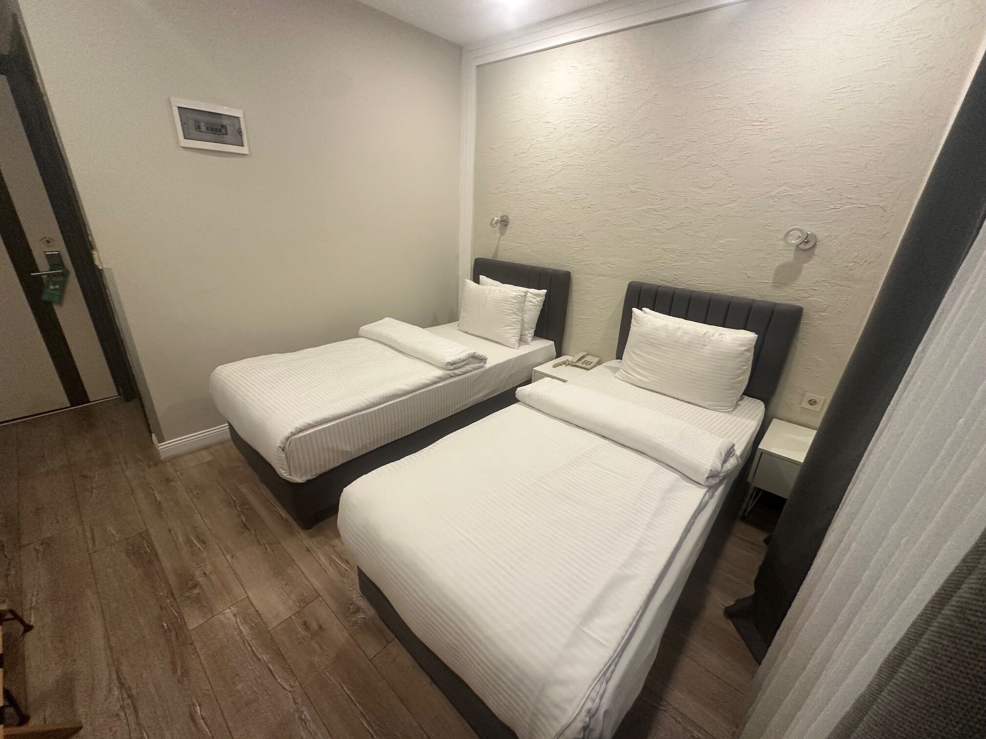 A hotel room with two beds, a small bedside table with a phone, and a wall-mounted light fixture.