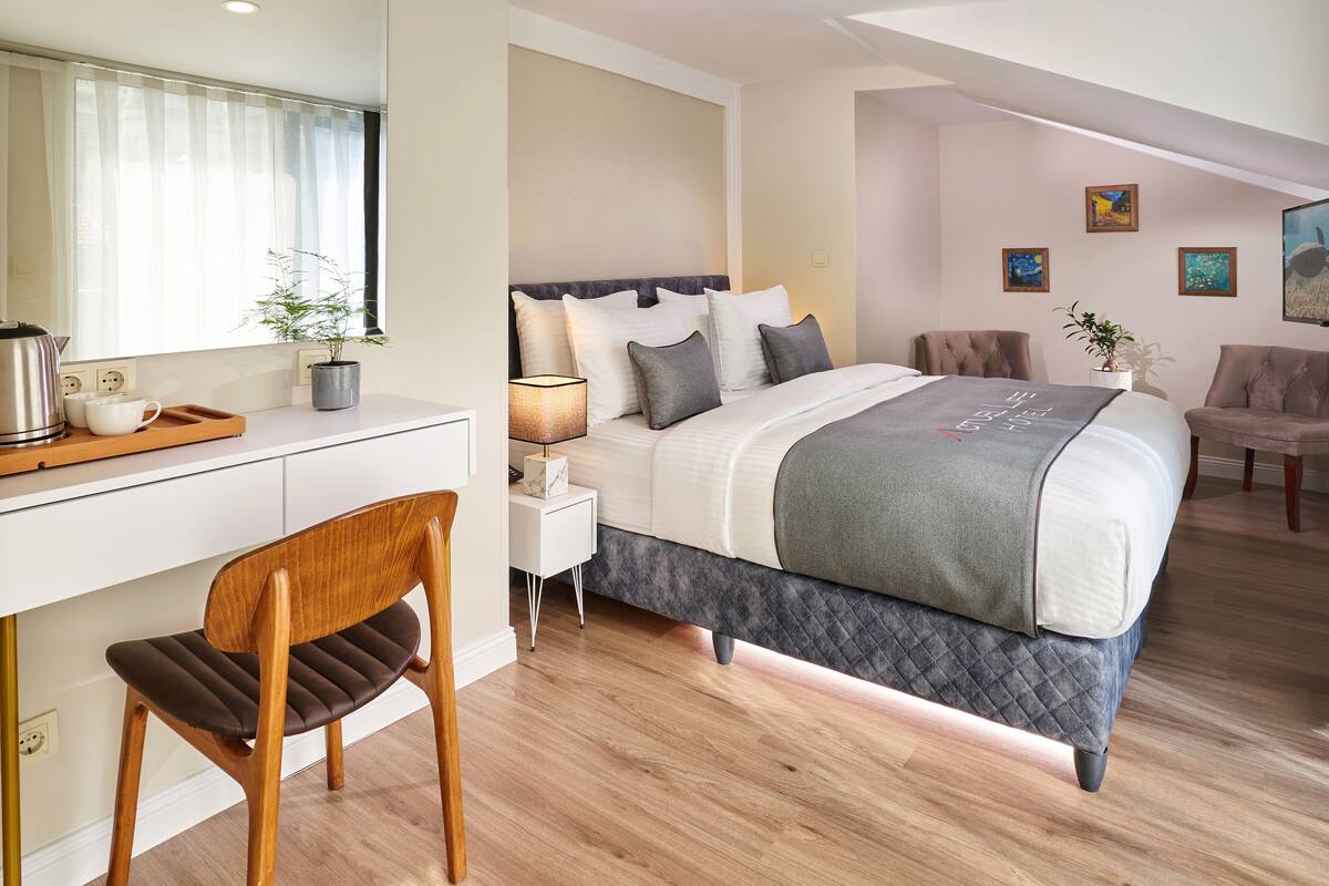 A modern hotel room with a bed, bedside table, chair, and a desk with a chair.