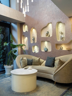 A modern living room with a beige sofa, a round coffee table, and decorative wall niches with sculptures. - actuel life hotel (Istanbul)