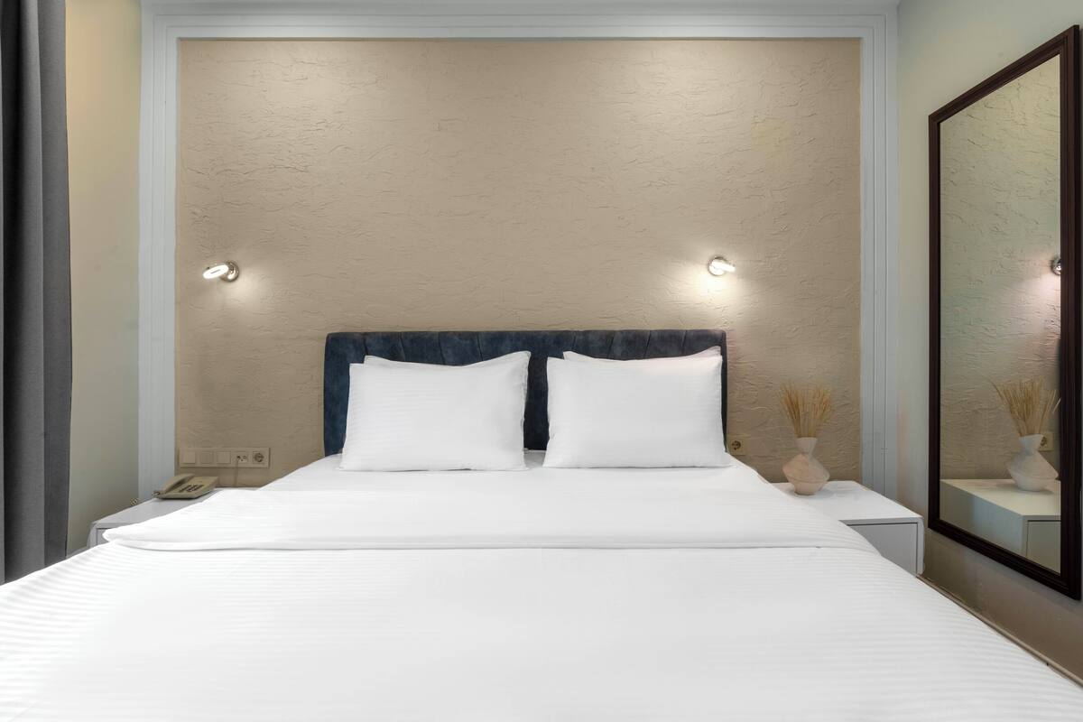 A neatly made bed with white linens, a dark headboard, and bedside lamps.