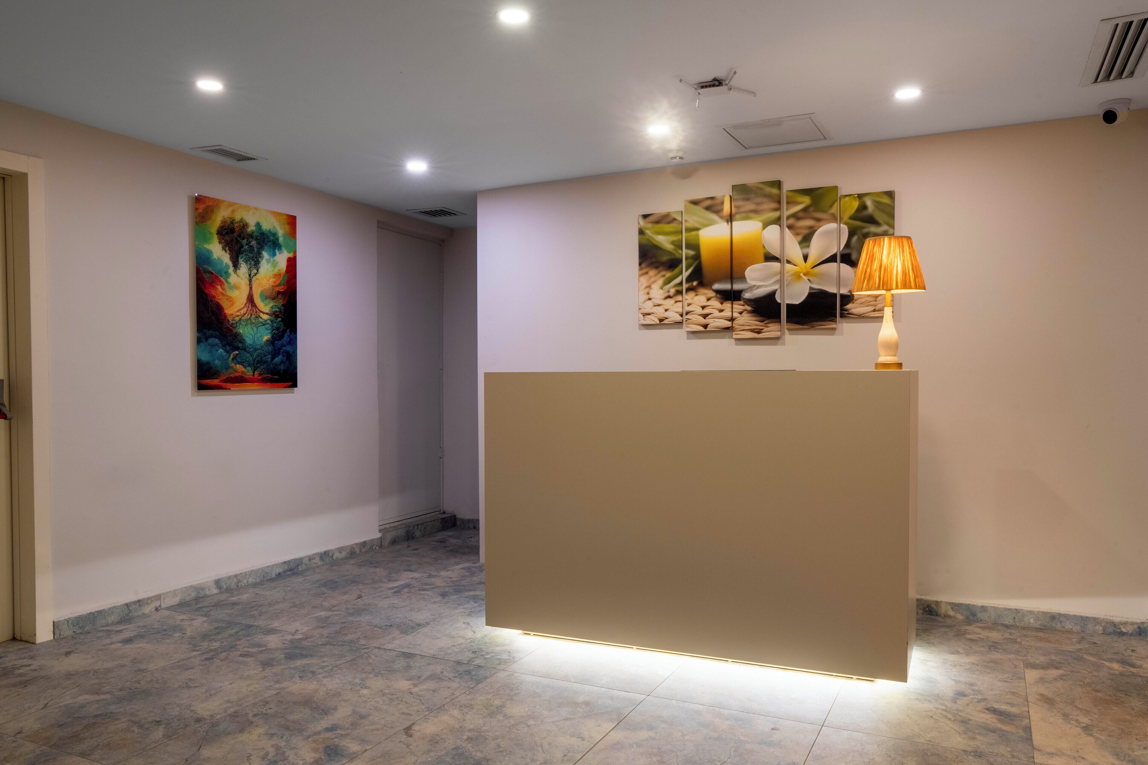 A reception area with a modern design, featuring a reception desk, a large abstract painting, and a set of framed floral photographs on the wall.