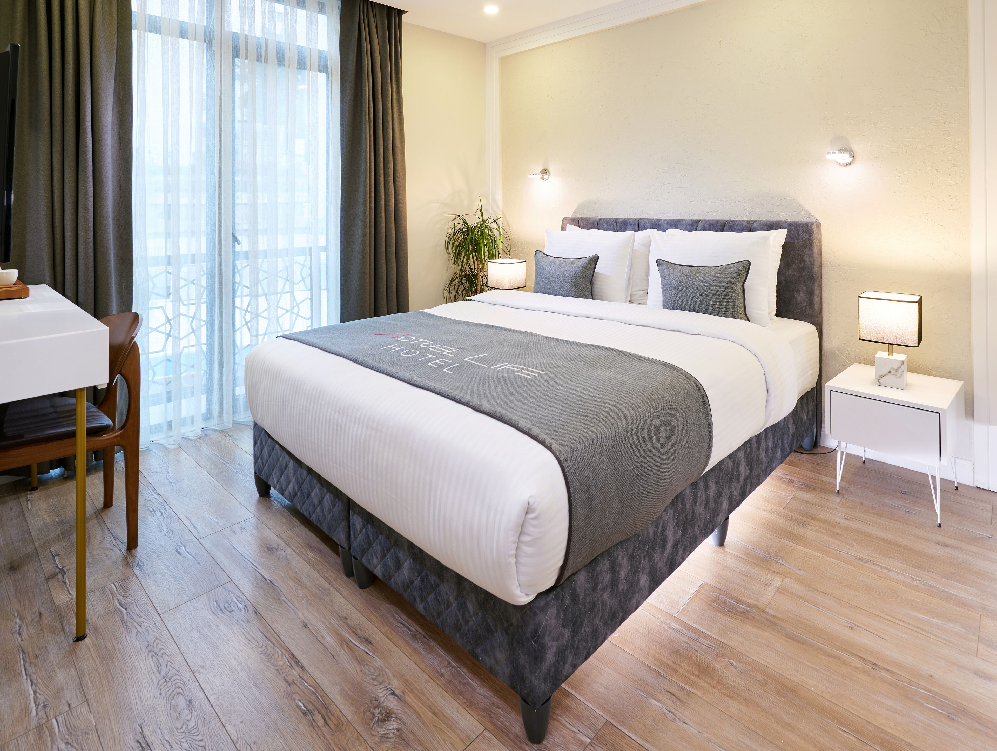 A hotel room with a bed, bedside tables, a desk, and a chair.