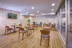 A modern cafe with wooden flooring, stone walls, and a variety of seating arrangements including tables and chairs. - actuel life hotel (Istanbul)