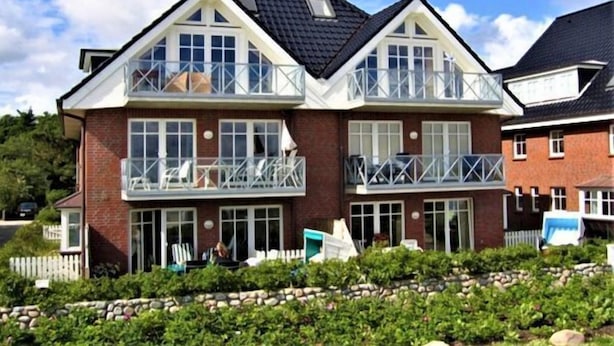 Une maison à deux étages avec un balcon à l’étage supérieur, une façade en briques et des fondations en pierre.