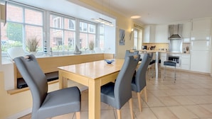 Une cuisine moderne avec des meubles blancs, un îlot central et un coin repas comprenant une table et des chaises en bois.