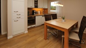 Una cocina compacta con armarios blancos, una mesa de comedor de madera y una ventana con cortinas.