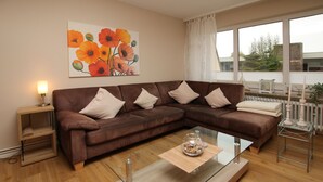 Un salón moderno con un sofá seccional marrón, una mesa de centro de vidrio y un cuadro de flores naranjas en la pared.