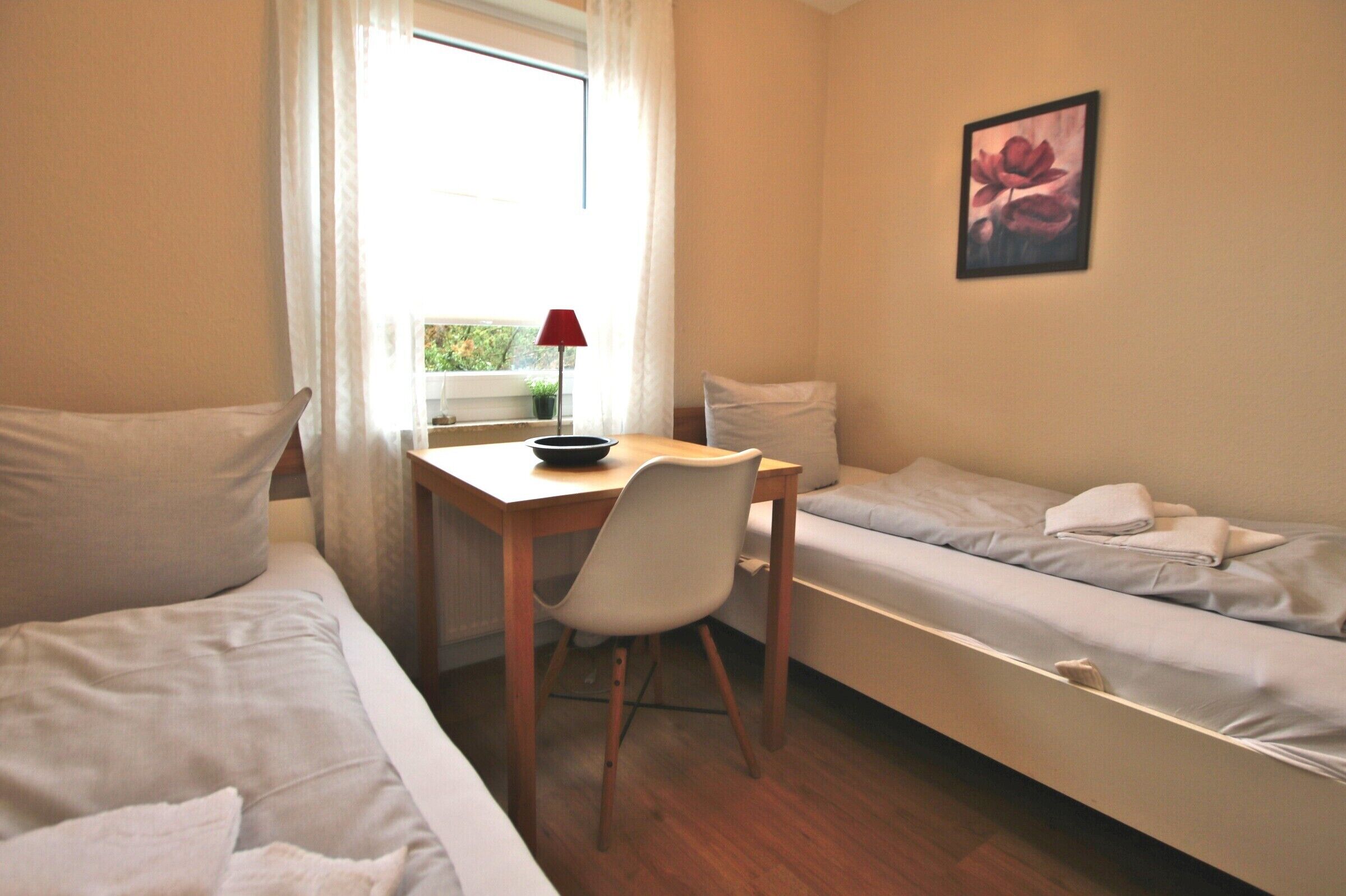 A small, well-lit room with a single bed, a desk with a chair, and a window with curtains.
