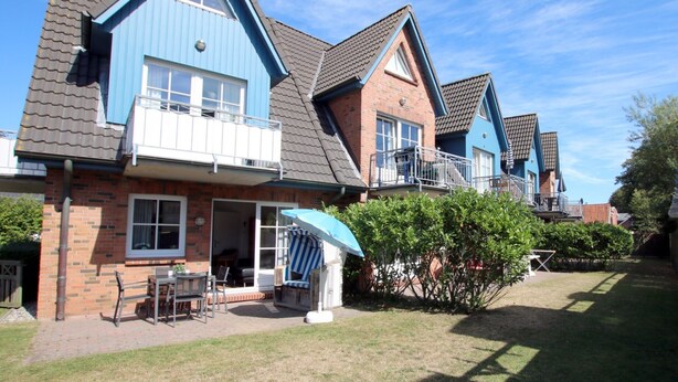 A residential building with a brick facade, blue accents, and a small patio area with outdoor furniture.