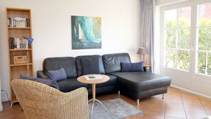 A modern living room with a sectional sofa, a round table, a bookshelf, and a painting of sailboats.