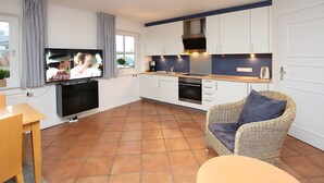 A modern kitchen with white cabinets, a built-in oven, and a television mounted on the wall.