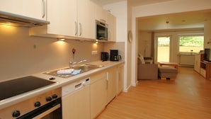 A modern kitchen with a stove, oven, microwave, and sink. There is a dining area with a table and chairs. - Ferienwohnung mit 3- Zimmern auf ca. 60m² im Erdgeschoß Eines Reihenhauses (Wyk auf Föhr)