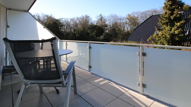 Een balkon met een tafel en stoelen, een witte leuning en uitzicht op bomen en gebouwen.