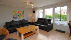 Un salon avec un canapé en cuir noir, une table basse en bois, un fauteuil en osier et un tableau abstrait aux couleurs vives accroché au mur.