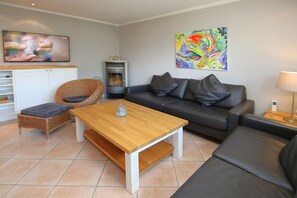 Un salon comprenant un canapé, une table basse en bois, un fauteuil en osier, une cheminée et un téléviseur.