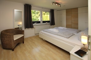 Une chambre à coucher comprenant un lit, une chaise, une table de chevet avec une lampe, une fenêtre avec des rideaux et une armoire.