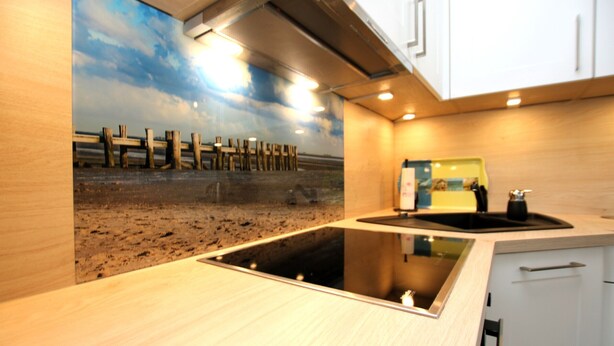 A kitchen with a wooden countertop, a built-in stove, and a wall mural of a beach scene. - Vacation apartment with 3 rooms on approx. 53m² (Wyk auf Föhr)
