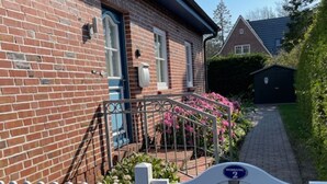 A brick house with a white picket fence, a paved pathway, and a small garden with pink flowers. - Vacation apartment with 3 rooms on approx. 53m² (Wyk auf Föhr)
