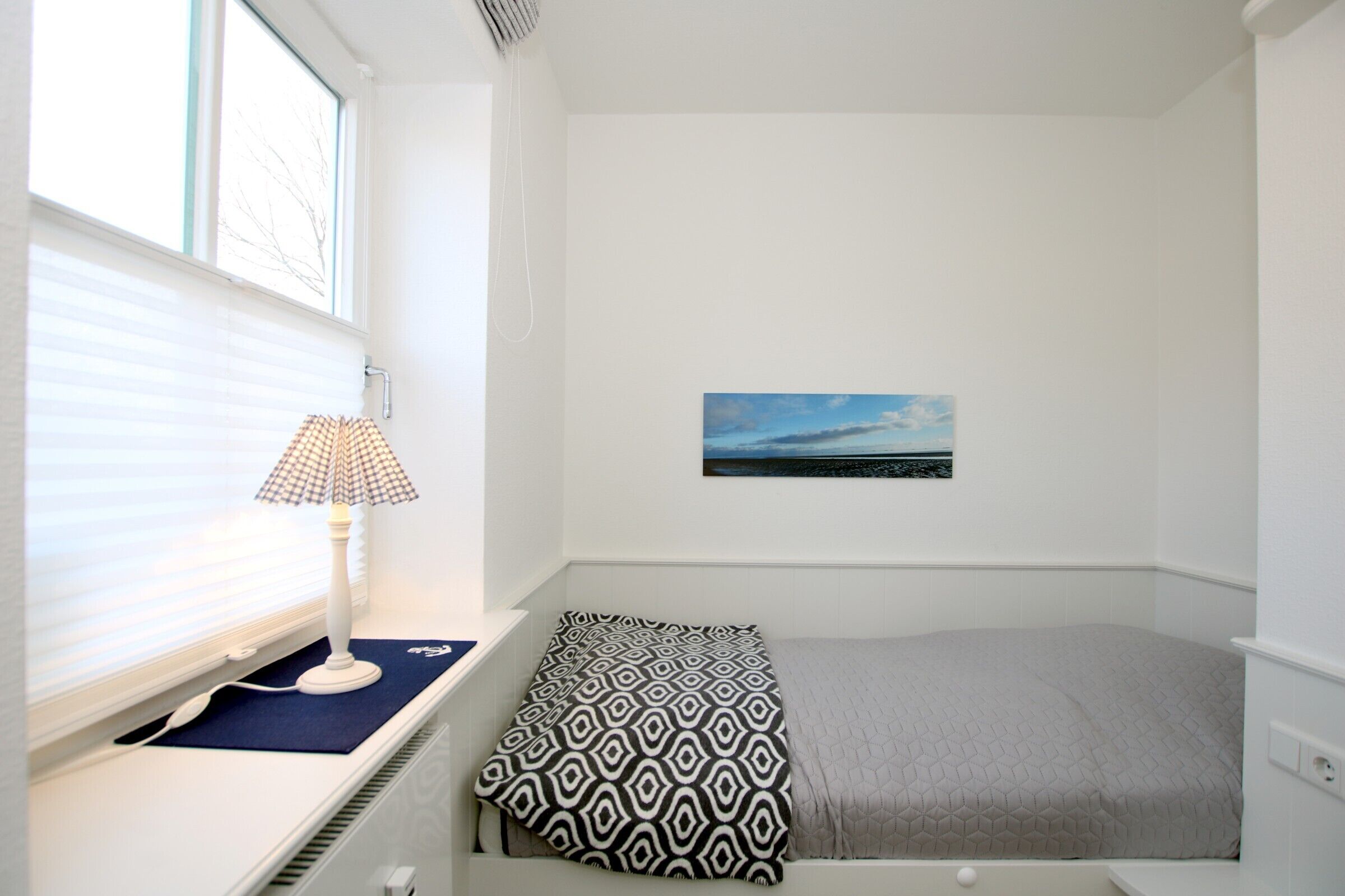 A bedroom with a bed, a window with blinds, a lamp, and a painting on the wall.
