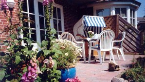A patio with white wicker chairs, a table, and a blue-striped umbrella. - Vacation apartment with 3 rooms on approx. 53m² (Wyk auf Föhr)